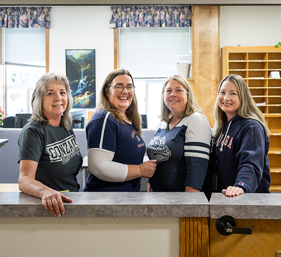 Four women wearing Gonzaga gear stand in a row through a window.